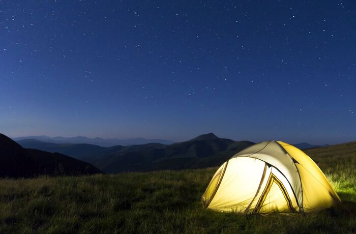 Tourist hikers tent in mountains at night with stars in the sky